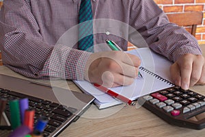 Man hand using calculator and writing make note with calculate about cost at home office. The Man and computer are using a calcula