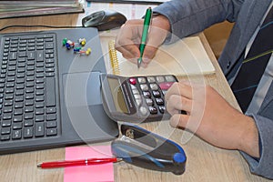 Man hand using calculator and writing make note with calculate about cost at home office. The Man and computer are using a calcula