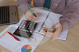 Man hand using calculator and writing make note with calculate about cost at home office. The Man and computer are using a calcula