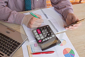 Man hand using calculator and writing make note with calculate about cost at home office. The Man and computer are using a calcula