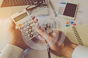 Man hand using a financial calculator and Financial data analyzing on desk at home