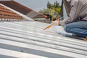 Man hand using glue gun with silicone adhesive or manual caulking gun with polyurethane to fix the metal steel on the roof.