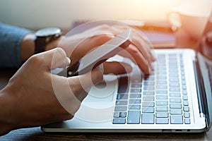 Man hand using mobile phone and typing keyboard of laptop computer on office desk.