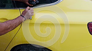 Man hand washing a yellow sports car before painting with a sponge and bucket of water focusing on the rear side