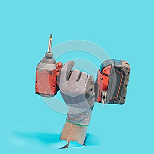 Man hand wearing a glove holds brushless cordless impact driver that breaks through blue ground