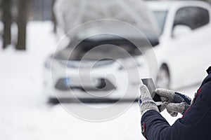 man hand in woolen gloves holding blank screen smart phone. Broken car in background