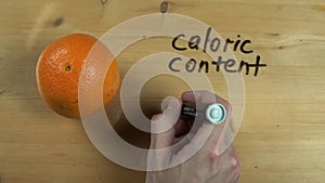 Man hand writes down caloric content of orange on wooden surface