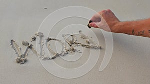 A man hand writes the word WORK on the sand and flushes the letters with a wave