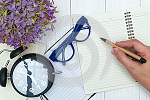 Man hand writing on blank page of notebook paper with pen, glasses and office supplies, top view