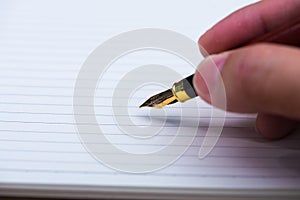 Man hand writing with fountain pen or ink pen with notebook paper on wooden working table with copy space, office desk concept.