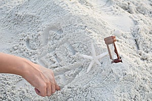 Man hand writing sea word on sand with shell