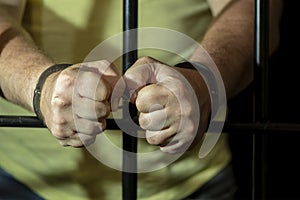 A man in handcuffs in a cell behind bars. Concept: a prisoner in a courtroom, a court sentence to a convicted person, a prison ter