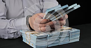 A man with handcuffs on his hands sits and holds stacks of dollars. A male official was arrested for taking a bribe of a