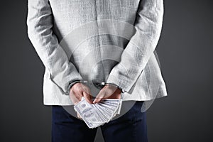 Man in handcuffs holding bribe money on background, closeup