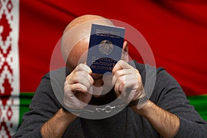 A man in handcuffs holds his passport against the background of the Belarusian flag. Concept: illegal detentions and arrests