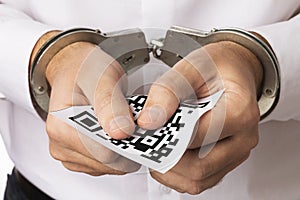 A man in handcuffs holds a sheet with a barcode, the concept of punishment for forgery of QR codes