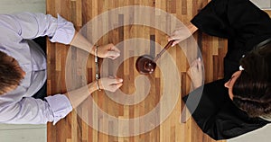 Man in handcuffs and a judge with gavel in courtroom top view