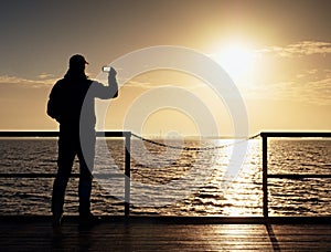 Man at handrail on mole take photos over sea to morning horizon. Tourist photograph