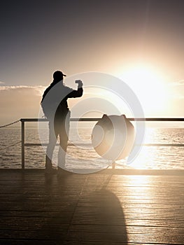 Man at handrail on mole take photos over sea to morning horizon. Tourist photograph