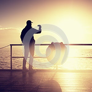 Man at handrail on mole take photos over sea to morning horizon. Tourist photograph