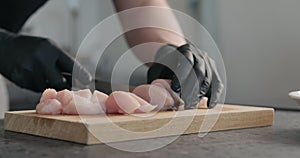 Man hands in black gloves cutting chicken fillet on oak board