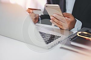 Man hands in black suit sitting and holding credit card and using laptop computer on table for online payment or shopping online.