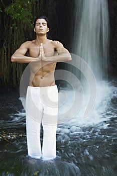 Man With Hands Clasped Meditating Against Waterfall