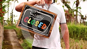 Man hands with closed sign board on a tropical nature background. Bali island.