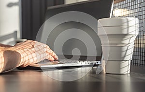 Man hands closeup typing on laptop keyboard. Businessman or student sitting at table with computer and takeaway eco