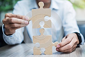 Man hands connecting couple puzzle over table, businessman holding wood jigsaw inside office. Business solutions, mission, target