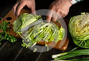 A man hands cut cabbage with a knife on a kitchen cutting board. The idea of shredding cabbage at home
