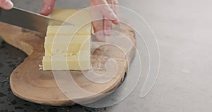 Man hands cut cheddar cheese in cubes on olive wood board