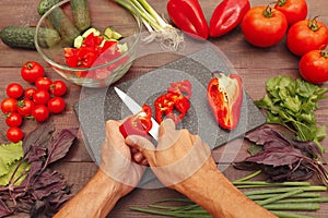Man hands cut fresh bellpepper for salad on wooden table photo