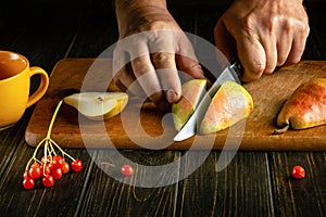 A man hands cut a ripe pear with a knife on a cutting board to prepare compote or fruit juice. Sweet pears for a set of vitamins