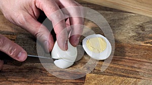 Man hands Cutting Boiled Egg on Wooden Board With Knife.