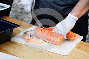 Man hands cutting pink raw salmon with knife on board