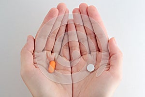 Man hands giving two big pills. White and orange. Make your selection. Health or ill.