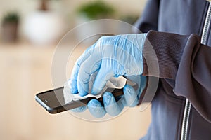 Man hands in gloves disinfecting smartphone, eliminating germs coronavirus bacteria