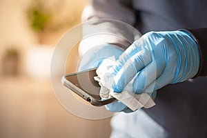 Man hands in gloves disinfecting smartphone, eliminating germs coronavirus bacteria