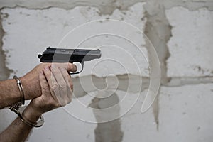 Man hands in handcuffs hold gun and ready to shoot on a grey wall background. Copy space