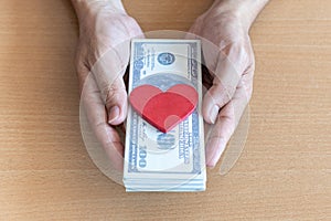 Man hands holding 100 dollar bills and red heart on wooden table. gives donation money to heart donors Concept