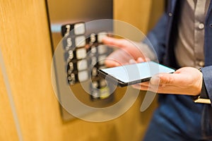 Close up of businessman using blank screen smartphone and pressing elevator button. Business and office building meeting concept