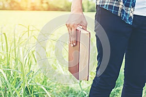 Man hands holding books on green meadow.