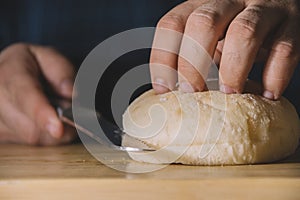 Man hands holding a bread bun and cutting it with a serrated stainless steel knife on a wooden board. Cooking concept