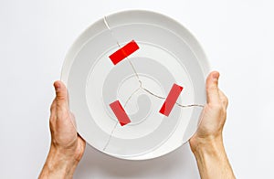 Man hands holding a broken white plate, parts glued with red tape. Metaphor for divorce, relationships, friendships, crack in