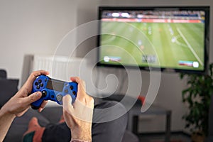 Man hands holding joystick and playing video game at home on coach sofa in front of television with play game concole