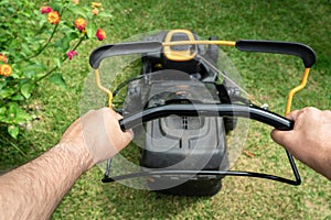 Man hand holding a lawn mower machine to cutting green grass