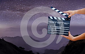 Man hands holding movie clapper on Milky Way , Stars and mountains. Shown slate board. use the colors white and black. Realistic m