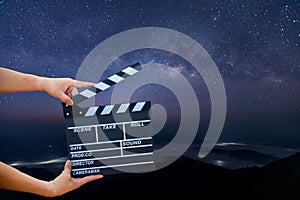 Man hands holding movie clapper on Milky Way , Stars and mountains. Shown slate board. use the colors white and black. Realistic m