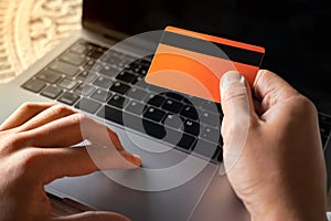 Man hands holding orange credit card and using laptop computer. Online shopping, e-commerce, online payment